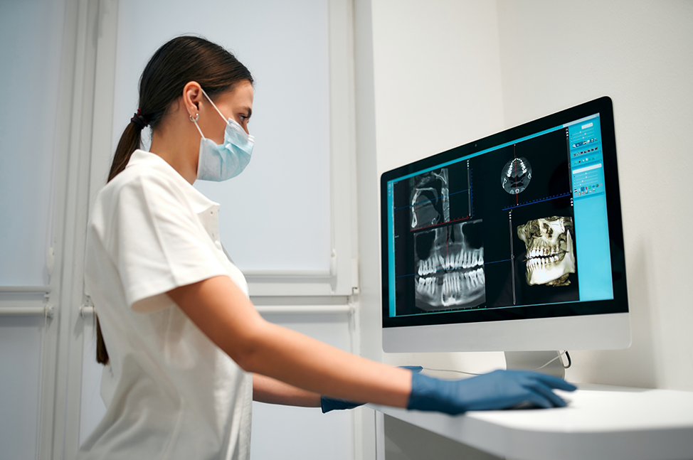 Dentist looking at several scans and x rays of a patients teeth and jaws on a computer